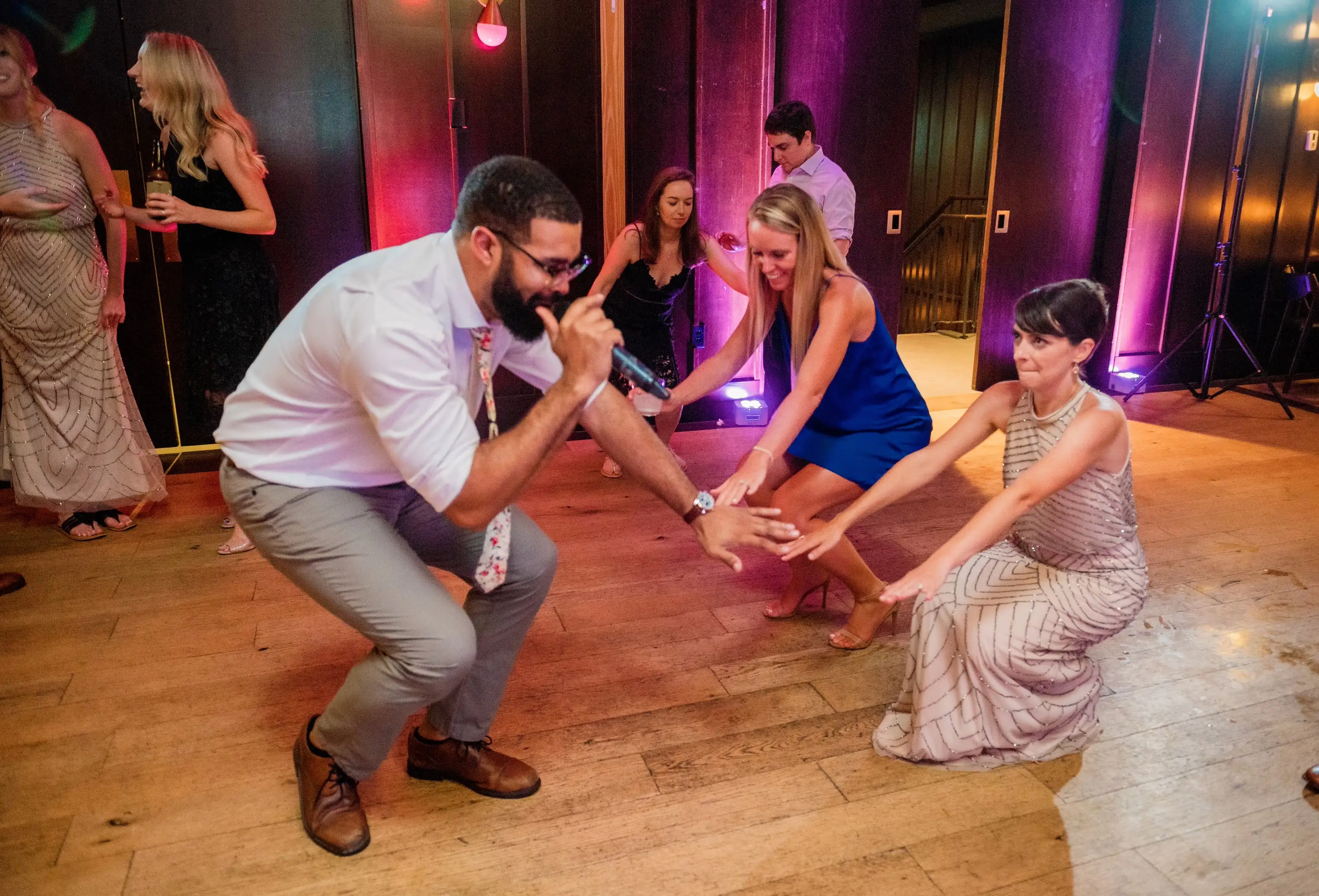 Guests dancing low on a dance floor lit in pink and purple