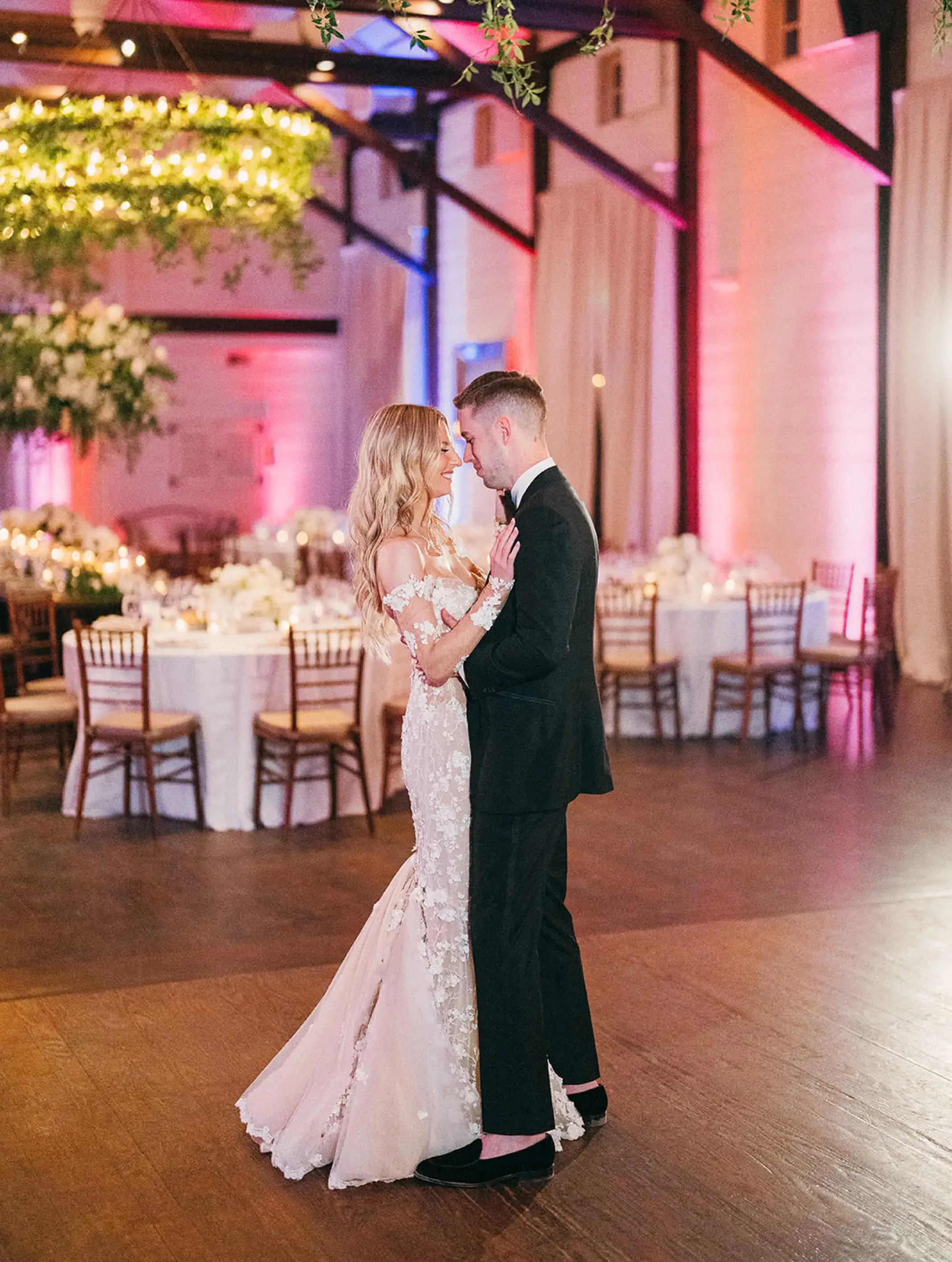 A bride and groom sharing a first dance in a hall washed in pink and blue uplighting